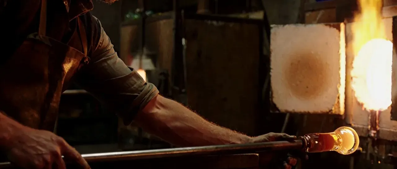 AI-generated frame: a glassblower shaping glowing glass at a furnace